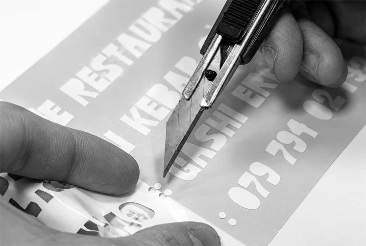 Découpe manuelle d’un lettrage adhésif par Décora Publicité à Genève